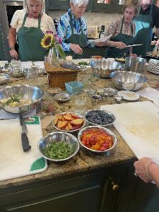 bowls of blueberries, peaches, and herbs placed by cutting boards and people cooking in the background at the teaching kitchen