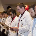 Crowd in white coats stands and reads from cards