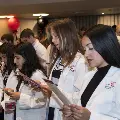 Crowd in white coats stands and reads from cards