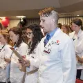 Crowd in white coats stands and reads from cards