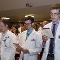 Crowd in white coats stands and reads from cards