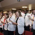 Crowd in white coats stands and reads from cards